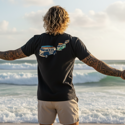 Person standing on a beach with arms outstretched, wearing a black t-shirt with a graphic design.